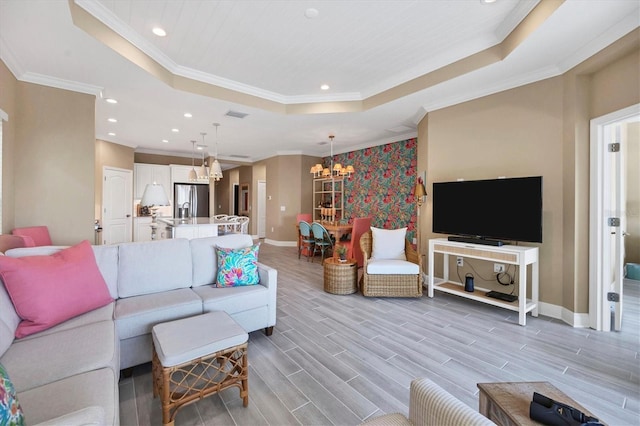 living room featuring an inviting chandelier, a tray ceiling, and ornamental molding