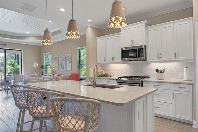 kitchen with pendant lighting, white cabinets, appliances with stainless steel finishes, an island with sink, and a breakfast bar area