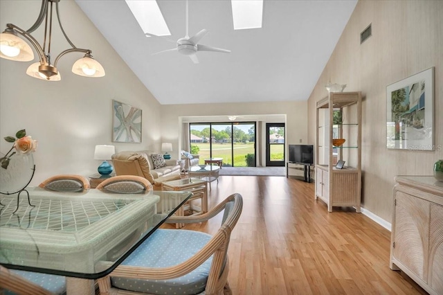 dining room featuring ceiling fan with notable chandelier, light hardwood / wood-style floors, high vaulted ceiling, and a skylight