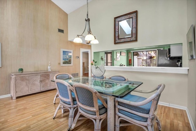 dining space featuring an inviting chandelier, light hardwood / wood-style floors, high vaulted ceiling, and wood walls