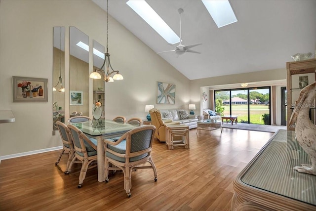 dining room featuring high vaulted ceiling, ceiling fan with notable chandelier, light hardwood / wood-style floors, and a skylight