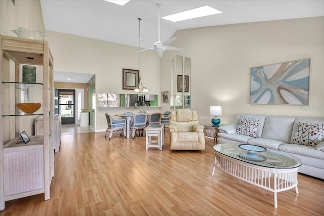 living room featuring ceiling fan, high vaulted ceiling, a skylight, and hardwood / wood-style floors