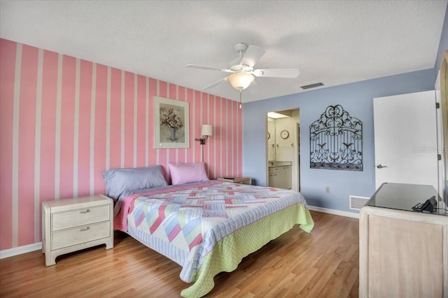 bedroom with ceiling fan, light hardwood / wood-style floors, a textured ceiling, and ensuite bathroom