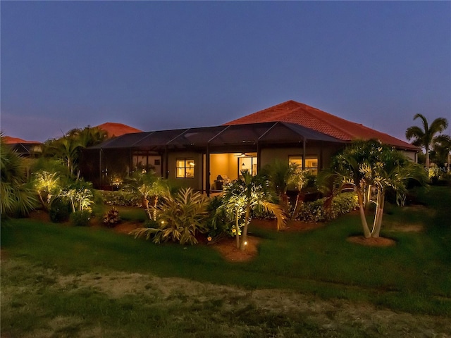 back house at dusk featuring glass enclosure and a yard