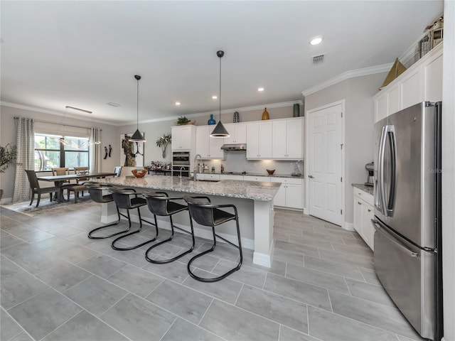 kitchen with decorative light fixtures, white cabinetry, stainless steel fridge, and a kitchen island with sink