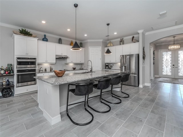 kitchen with white cabinets, french doors, an island with sink, and stainless steel appliances