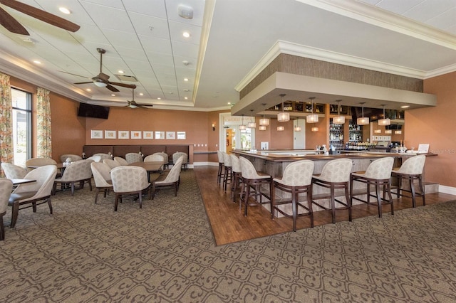 carpeted dining room with ceiling fan, ornamental molding, and indoor bar