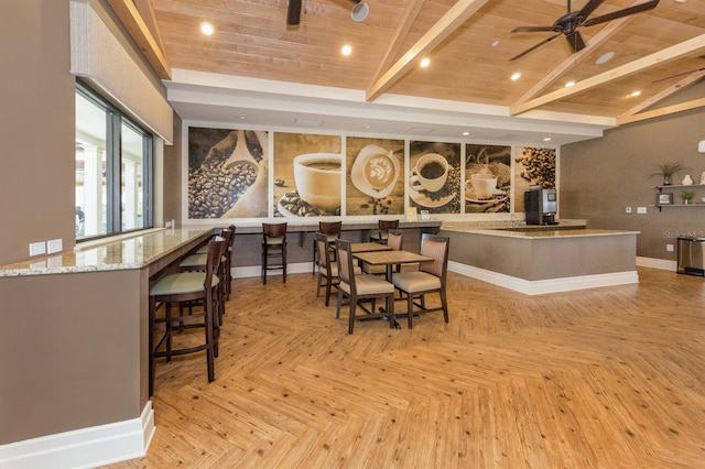 interior space with ceiling fan, light parquet flooring, vaulted ceiling with beams, light stone counters, and wooden ceiling