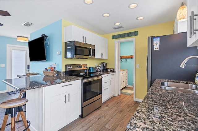 kitchen featuring white cabinetry, sink, a kitchen bar, stainless steel appliances, and light hardwood / wood-style flooring