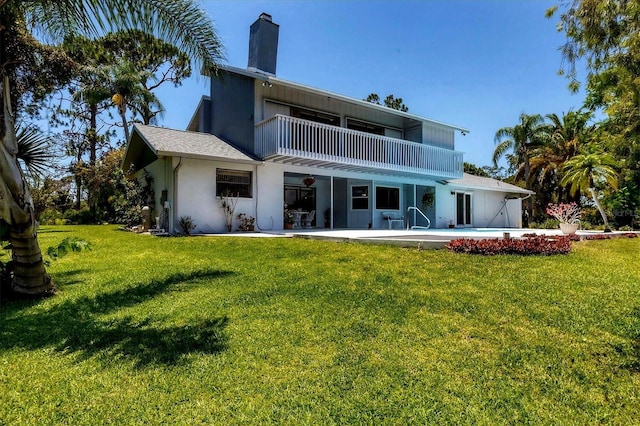 back of house featuring a patio, a balcony, a yard, and a chimney