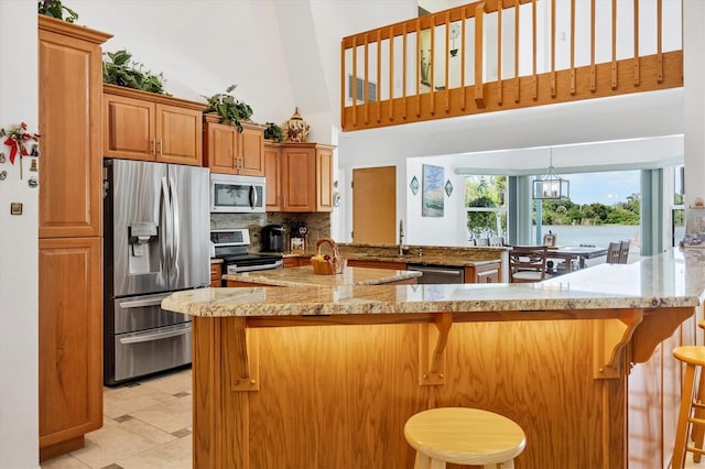 kitchen with decorative backsplash, a kitchen breakfast bar, appliances with stainless steel finishes, a high ceiling, and a peninsula