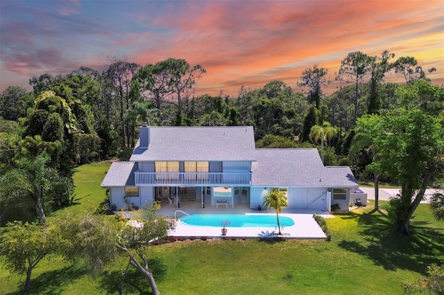 back of house at dusk featuring a patio, a lawn, an outdoor pool, and a chimney