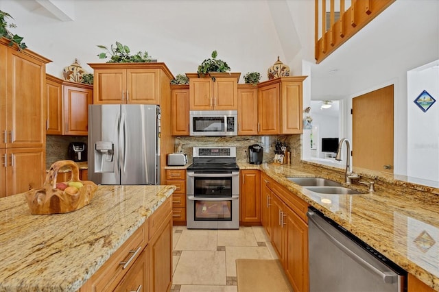 kitchen with light stone counters, decorative backsplash, appliances with stainless steel finishes, a high ceiling, and a sink