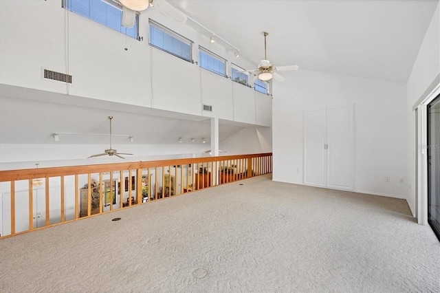 carpeted empty room featuring visible vents, rail lighting, high vaulted ceiling, and a ceiling fan