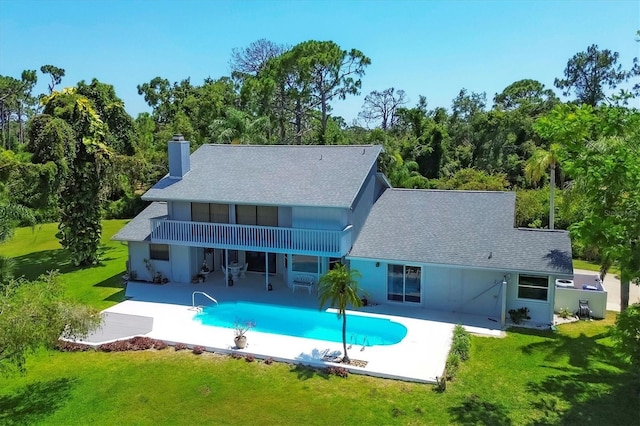 rear view of house featuring a lawn, roof with shingles, an outdoor pool, a chimney, and a patio area