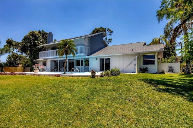 rear view of property with a balcony, a patio area, fence, and a lawn