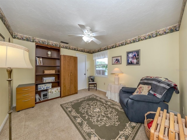 living area featuring ceiling fan, light carpet, and a textured ceiling