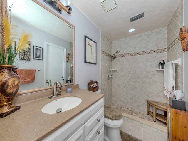 bathroom with a tile shower, tile patterned flooring, vanity, and toilet