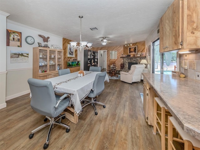 dining space featuring a stone fireplace, crown molding, ceiling fan, a textured ceiling, and wood-type flooring