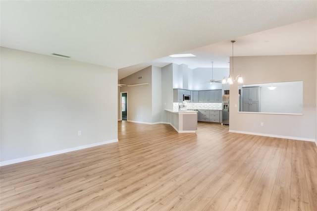 unfurnished living room featuring light hardwood / wood-style flooring, high vaulted ceiling, ceiling fan with notable chandelier, and sink