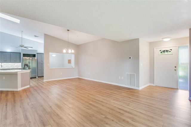 unfurnished living room with ceiling fan with notable chandelier, light hardwood / wood-style floors, lofted ceiling, and sink