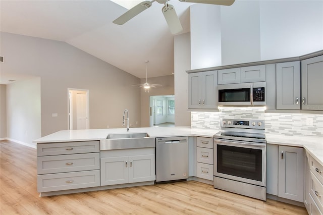 kitchen with gray cabinetry, sink, stainless steel appliances, lofted ceiling, and decorative backsplash