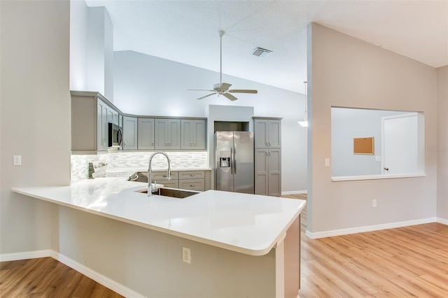 kitchen with kitchen peninsula, tasteful backsplash, stainless steel appliances, sink, and gray cabinets