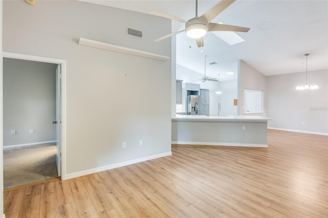 unfurnished living room featuring high vaulted ceiling, ceiling fan with notable chandelier, sink, a skylight, and light hardwood / wood-style floors