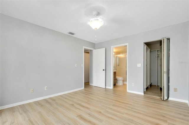 unfurnished bedroom featuring a closet, light hardwood / wood-style flooring, ensuite bath, and a spacious closet