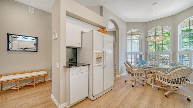 kitchen with white cabinetry, decorative light fixtures, dark stone counters, white refrigerator with ice dispenser, and light hardwood / wood-style floors