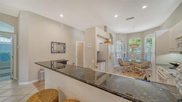 kitchen featuring a wealth of natural light, pendant lighting, white cabinetry, dark stone counters, and white refrigerator with ice dispenser