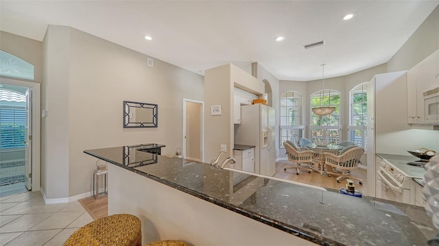 kitchen featuring recessed lighting, visible vents, baseboards, white fridge with ice dispenser, and dark stone countertops