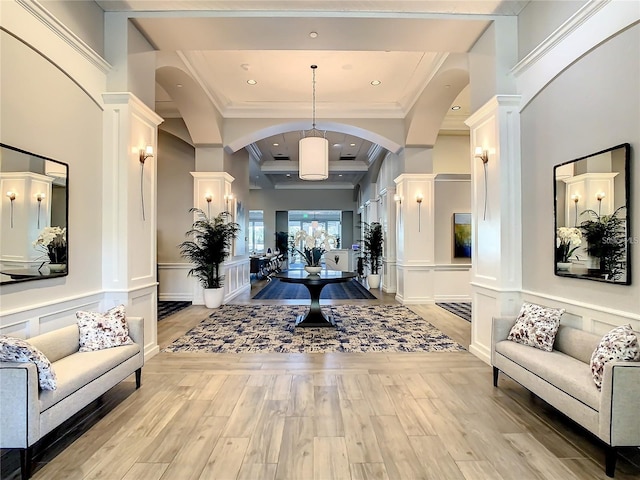 foyer featuring arched walkways, wainscoting, ornamental molding, light wood-style floors, and a decorative wall