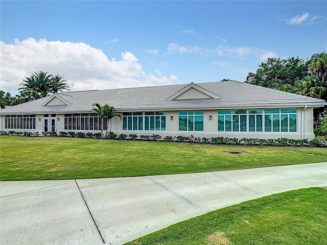 view of front facade with a sunroom, a tiled roof, a front lawn, and stucco siding