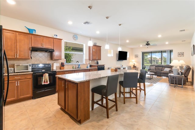 kitchen featuring black electric range oven, decorative light fixtures, a center island, a kitchen breakfast bar, and light stone countertops