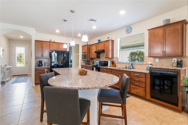 kitchen featuring decorative light fixtures, sink, a kitchen breakfast bar, a center island, and black appliances