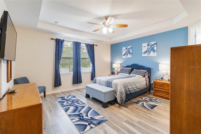 bedroom with ceiling fan, light hardwood / wood-style floors, and a tray ceiling