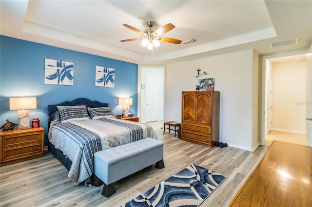 bedroom with ceiling fan, light hardwood / wood-style floors, and a tray ceiling