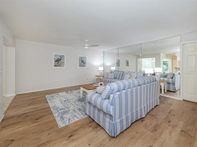 living room with light wood finished floors, a textured ceiling, a ceiling fan, and baseboards