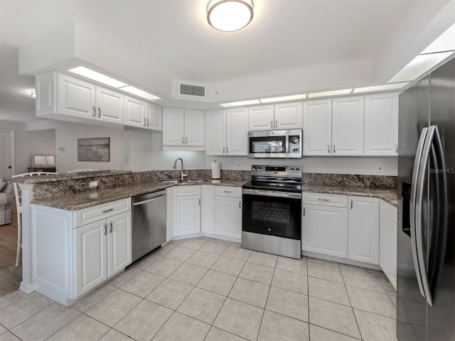 kitchen with dark stone countertops, appliances with stainless steel finishes, white cabinetry, sink, and kitchen peninsula