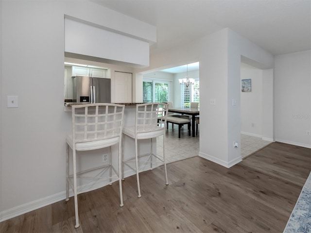 kitchen with a notable chandelier, a kitchen breakfast bar, wood finished floors, stainless steel fridge, and baseboards