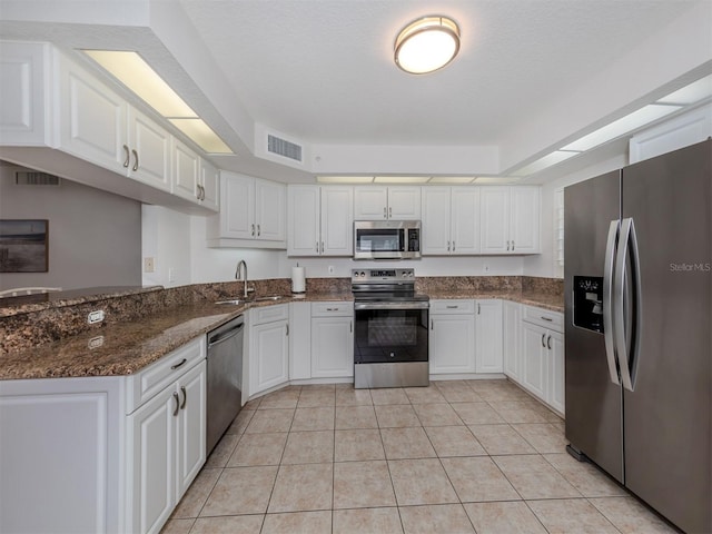 kitchen featuring dark stone countertops, light tile patterned floors, kitchen peninsula, appliances with stainless steel finishes, and white cabinets