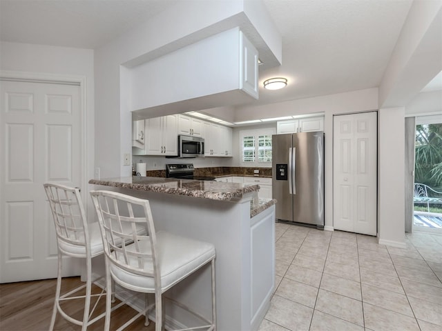 kitchen featuring kitchen peninsula, stainless steel appliances, white cabinetry, and a healthy amount of sunlight