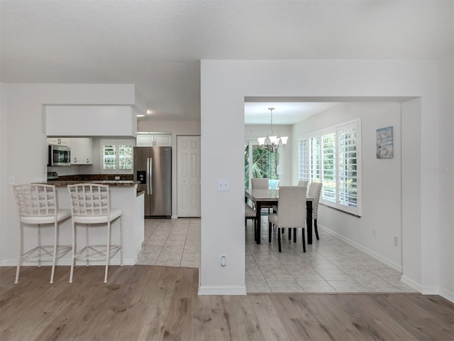 kitchen with light hardwood / wood-style flooring, hanging light fixtures, stainless steel appliances, kitchen peninsula, and white cabinetry