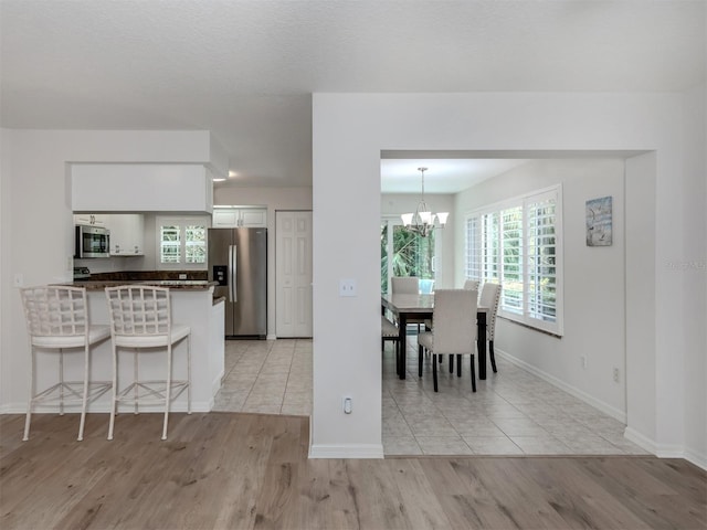 dining space with light wood-style flooring, baseboards, and an inviting chandelier