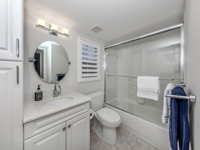 full bathroom featuring a textured ceiling, vanity, combined bath / shower with glass door, tile patterned flooring, and toilet