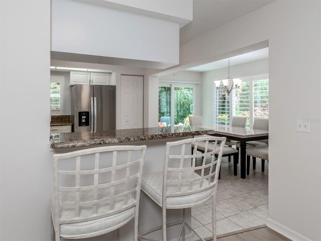 kitchen with white cabinetry, light tile patterned floors, decorative light fixtures, an inviting chandelier, and stainless steel refrigerator with ice dispenser