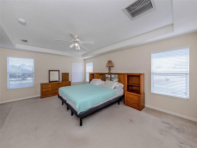 bedroom with ceiling fan, a tray ceiling, and light carpet