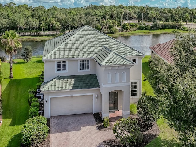 mediterranean / spanish home featuring decorative driveway, a tile roof, stucco siding, a water view, and a garage