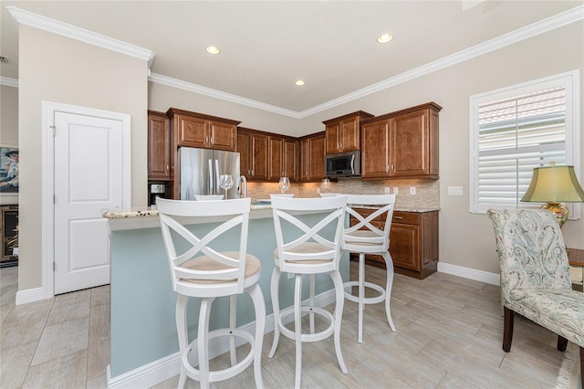 kitchen featuring decorative backsplash, appliances with stainless steel finishes, a kitchen bar, ornamental molding, and a kitchen island with sink